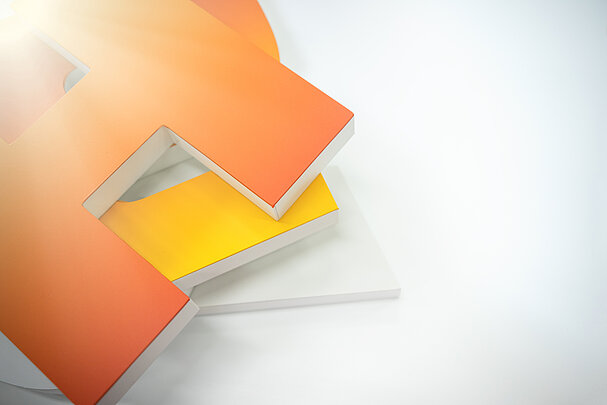 Farbige, aus dem Kunststoffprodukt SIMOPOR gefertigte Buchstaben in Orange und Gelb, die auf einer weißen Fläche platziert sind.