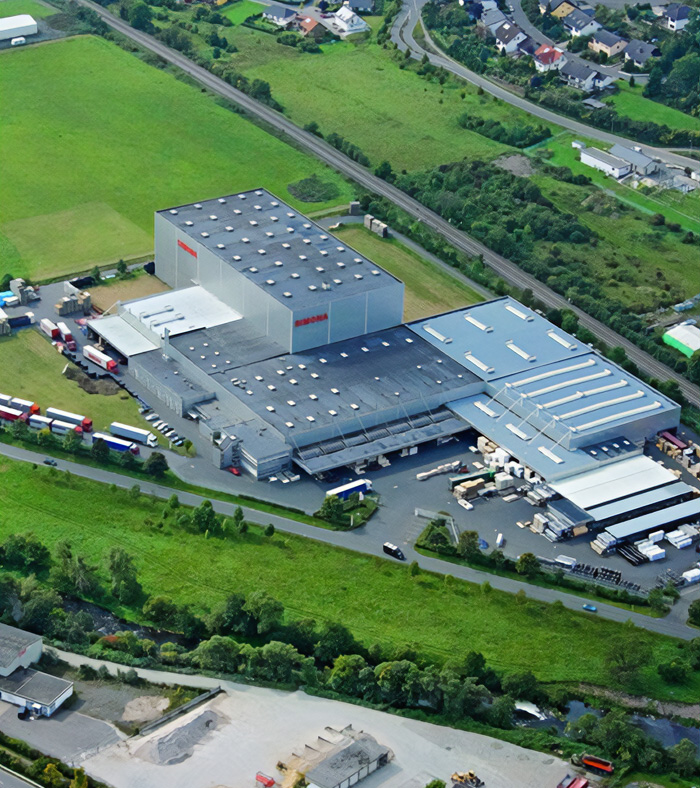 Luftaufnahme eines großen Industrie- und Logistikgebäudes mit angrenzenden Lagerflächen und Lkw-Stellplätzen. Es handelt sich um den SIMONA Unternehmensstandort.